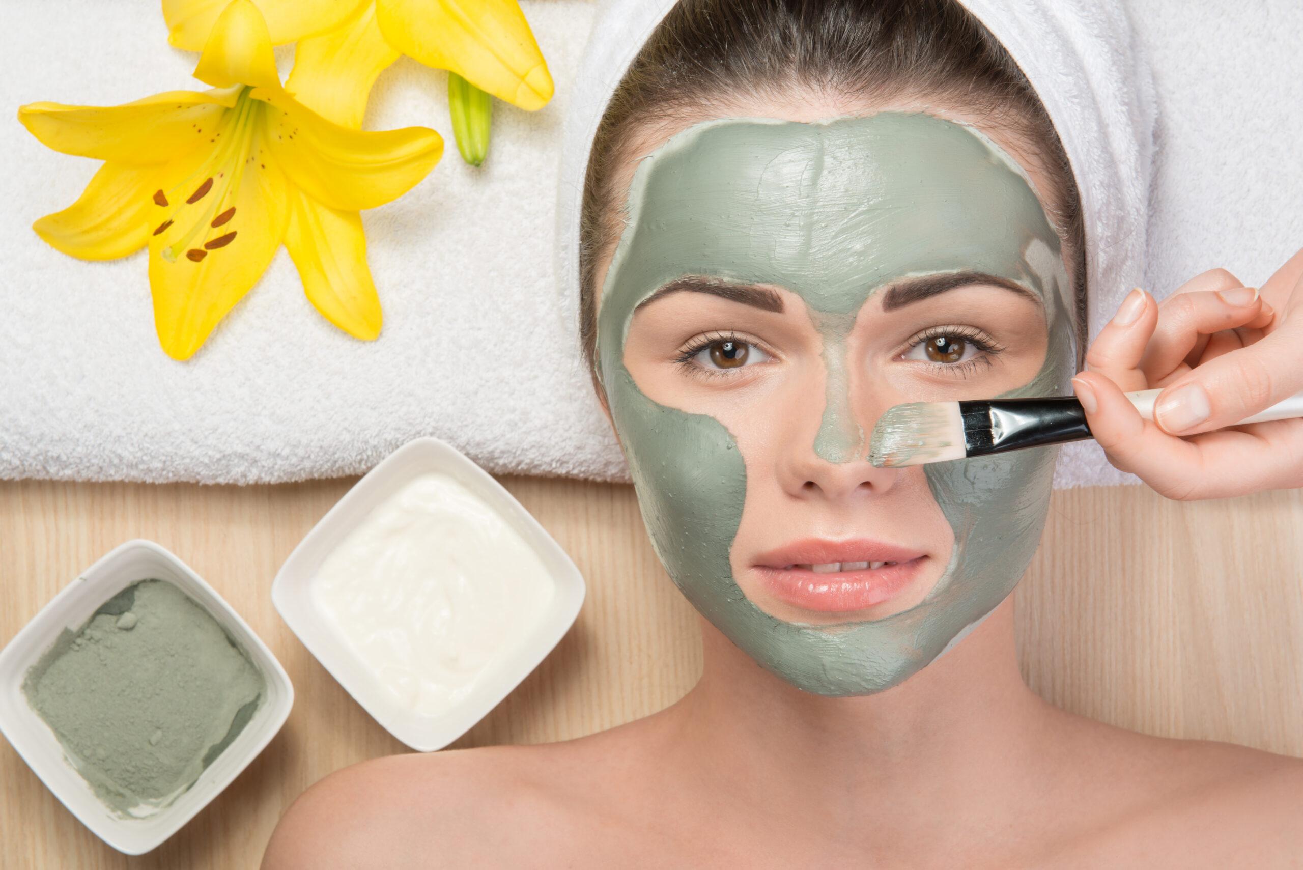 Beautiful girl with a towel on her head applying facial clay mas green peel scaled